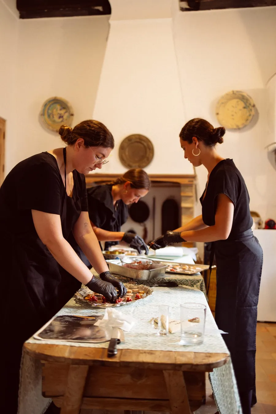 Tres integrantes del equipo emplatando canapés en una cocina de evento.