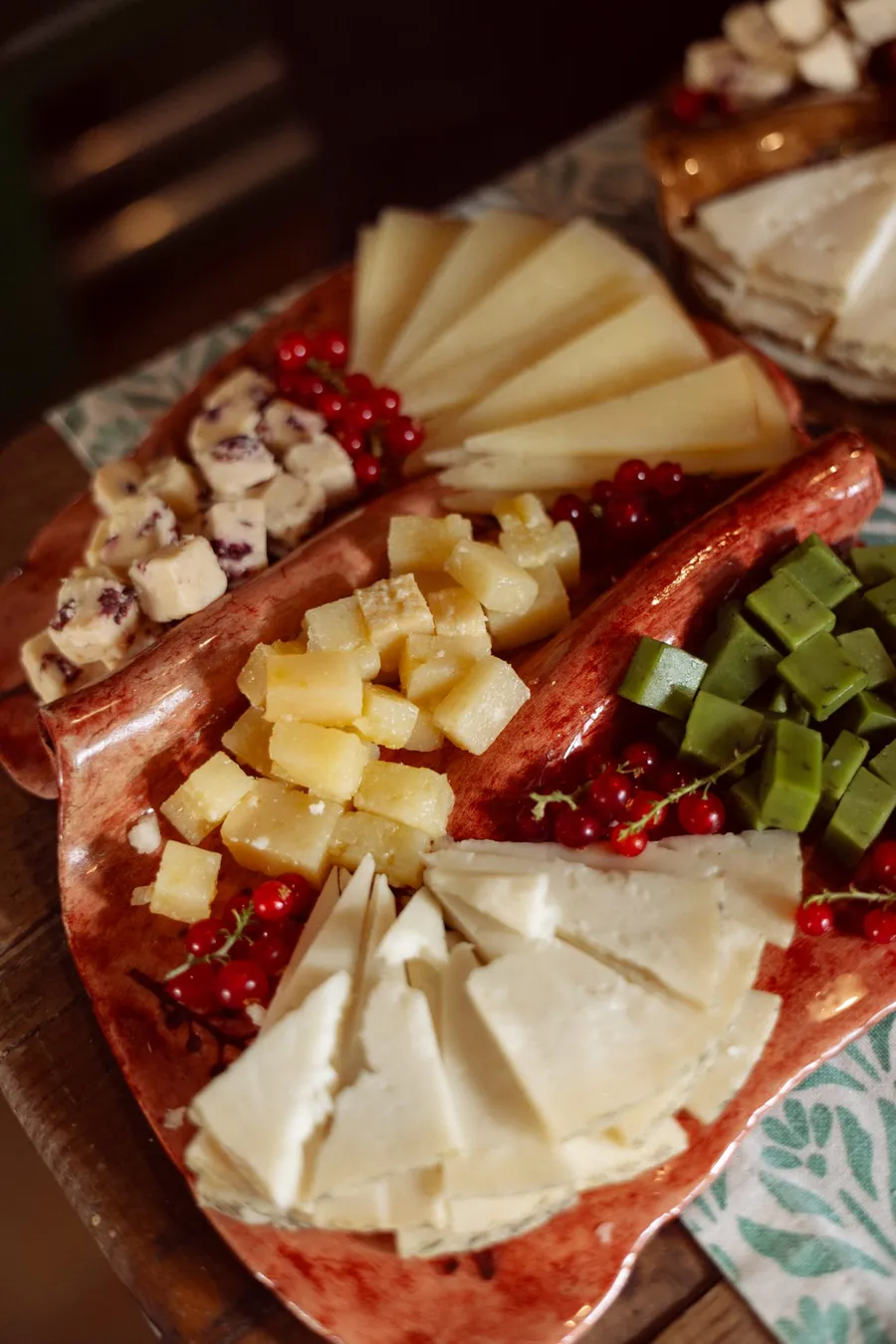 Tabla de quesos variados con frutos rojos, presentada en bandeja de cerámica.