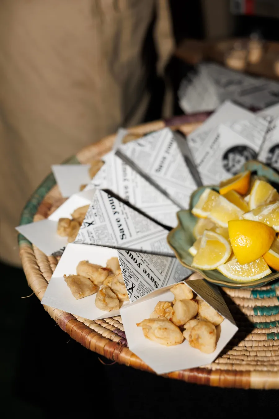 Pescaíto frito servido en cucuruchos de papel, con limón, en un evento al aire libre.